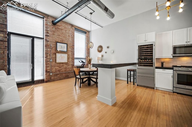 kitchen featuring stainless steel appliances, brick wall, a towering ceiling, white cabinetry, and dark countertops