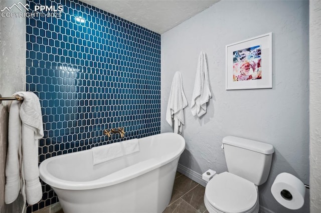 full bathroom featuring a textured ceiling, a textured wall, toilet, baseboards, and a freestanding bath