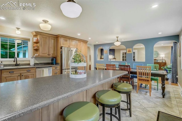 kitchen featuring a breakfast bar, open shelves, stainless steel appliances, dark countertops, and a sink