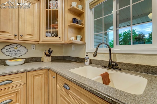 kitchen with glass insert cabinets, light brown cabinets, a sink, and open shelves