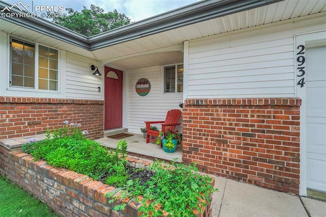 entrance to property featuring a garage, brick siding, and covered porch