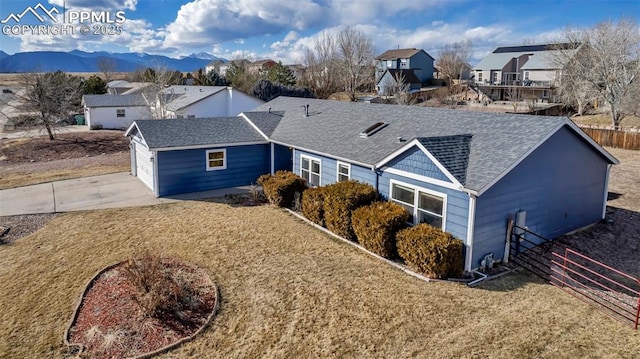 view of front of home with a mountain view, roof with shingles, fence, and a residential view