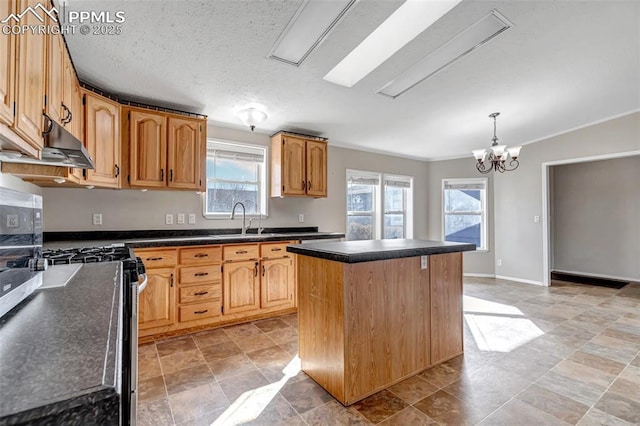 kitchen with pendant lighting, dark countertops, a kitchen island, a sink, and under cabinet range hood