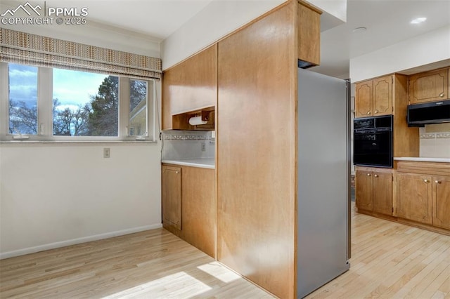 kitchen featuring brown cabinetry, freestanding refrigerator, oven, light countertops, and light wood-type flooring