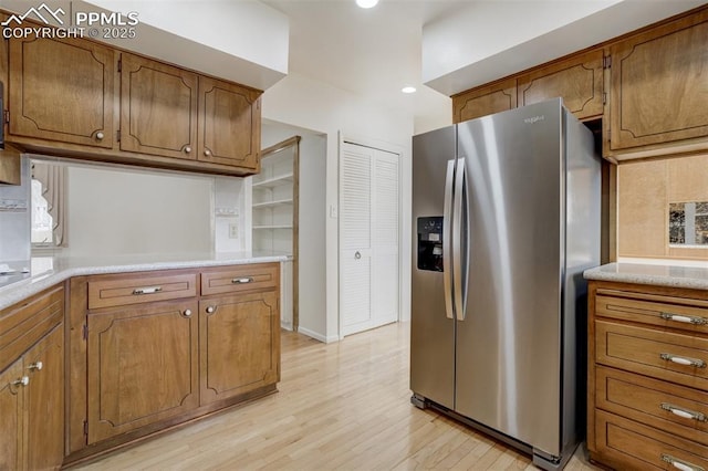 kitchen featuring light wood-style floors, stainless steel fridge, brown cabinets, and light countertops