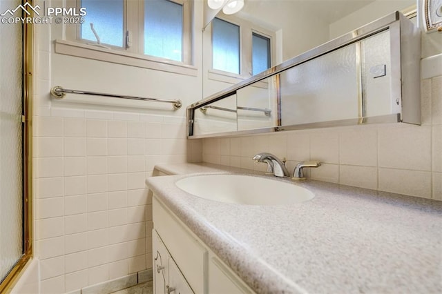 bathroom featuring a shower with shower door, plenty of natural light, tile walls, and vanity