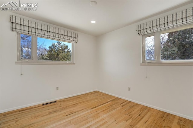 unfurnished room featuring light wood-style floors, a healthy amount of sunlight, visible vents, and baseboards