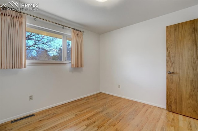 unfurnished room featuring wood finished floors, visible vents, and baseboards