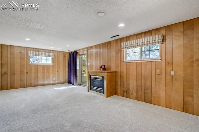 unfurnished living room with visible vents, a glass covered fireplace, a textured ceiling, carpet floors, and wood walls