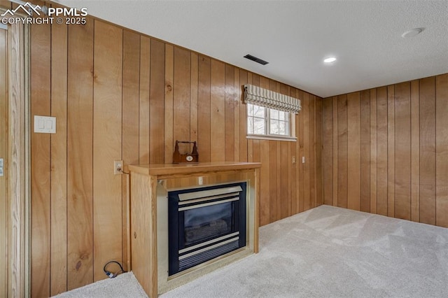 unfurnished living room featuring wood walls, carpet, a glass covered fireplace, and visible vents