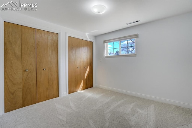 unfurnished bedroom with baseboards, carpet, visible vents, and two closets