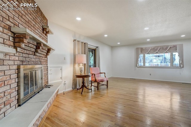 living area with a textured ceiling, recessed lighting, wood finished floors, baseboards, and a brick fireplace