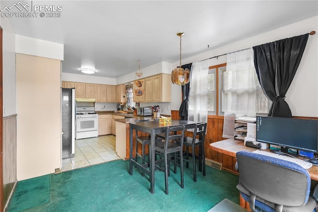 kitchen with light tile patterned floors, white range with gas stovetop, freestanding refrigerator, under cabinet range hood, and light brown cabinets