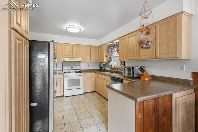 kitchen with dark countertops, appliances with stainless steel finishes, a peninsula, light brown cabinetry, and a sink