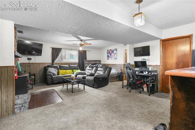 carpeted living area with a wainscoted wall, wooden walls, a ceiling fan, and a textured ceiling