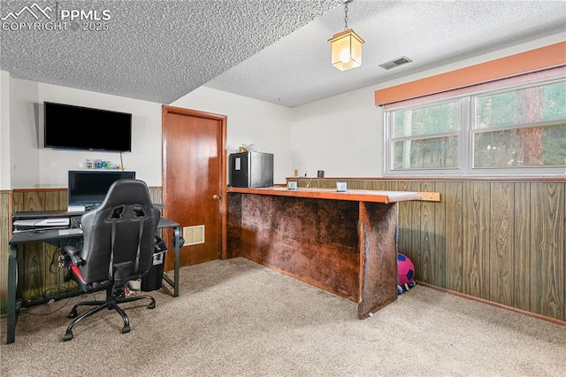 carpeted office space featuring visible vents, wood walls, and a textured ceiling