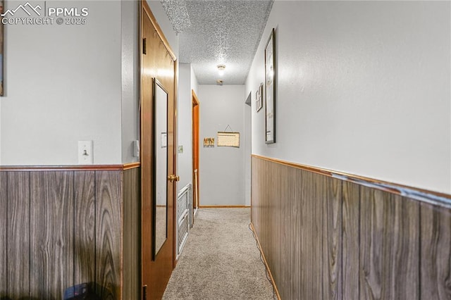 hall with wainscoting, wood walls, a textured ceiling, and light colored carpet