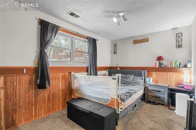 carpeted bedroom with a wainscoted wall, visible vents, wood walls, and a textured ceiling