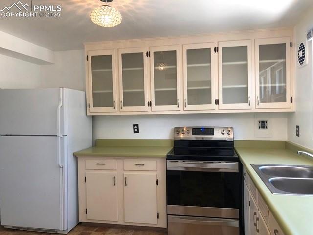 kitchen featuring light countertops, glass insert cabinets, freestanding refrigerator, stainless steel range with electric cooktop, and a sink