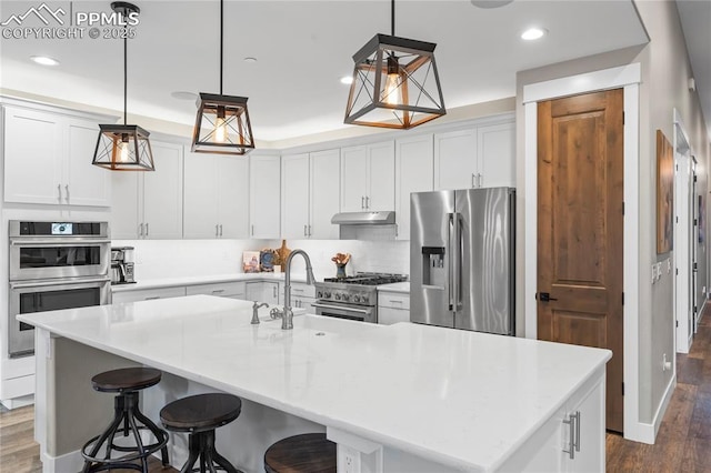 kitchen with dark wood finished floors, appliances with stainless steel finishes, light countertops, under cabinet range hood, and white cabinetry