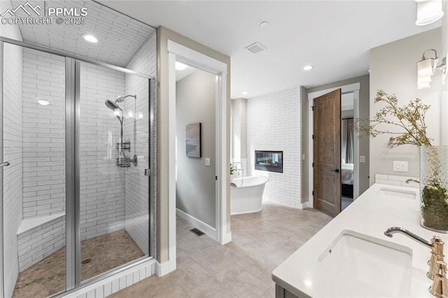 bathroom with a large fireplace, visible vents, a freestanding bath, a shower stall, and a sink