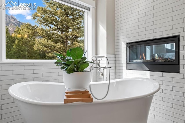 interior details featuring a soaking tub and a glass covered fireplace