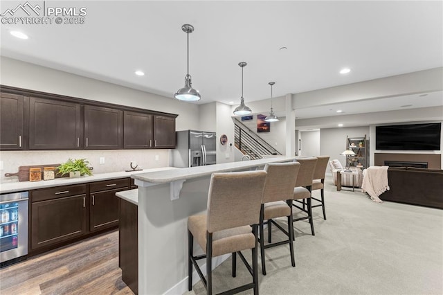 kitchen with dark brown cabinetry, stainless steel fridge, decorative backsplash, light countertops, and a kitchen bar