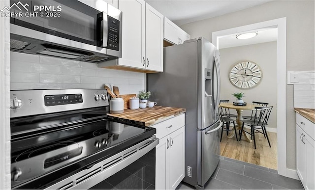 kitchen featuring butcher block counters, dark tile patterned floors, white cabinetry, appliances with stainless steel finishes, and tasteful backsplash