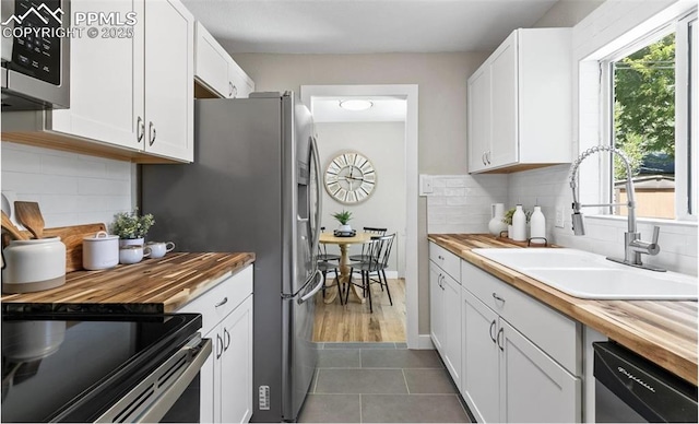 kitchen with stainless steel appliances, wooden counters, white cabinetry, a sink, and dark tile patterned floors