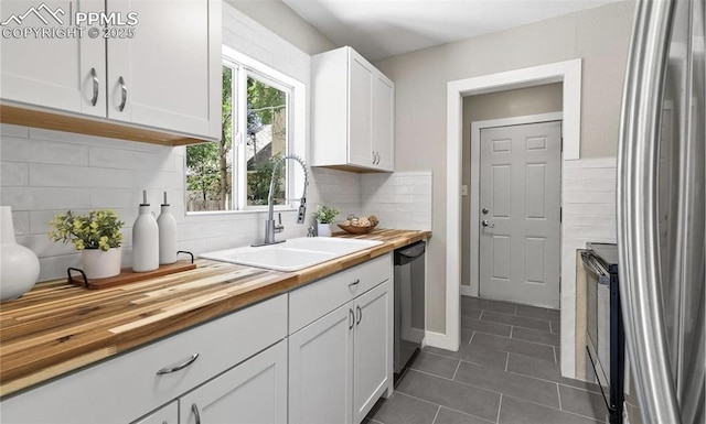 kitchen featuring butcher block counters, appliances with stainless steel finishes, white cabinetry, a sink, and dark tile patterned floors