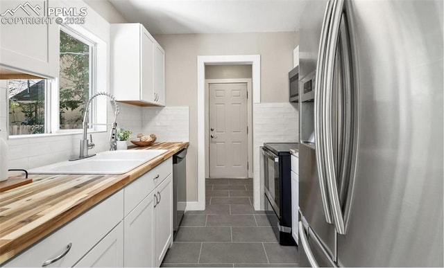 kitchen featuring white cabinets, stainless steel appliances, dark tile patterned floors, wooden counters, and a sink