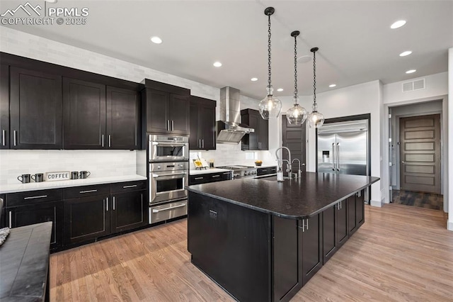 kitchen with visible vents, stainless steel appliances, wall chimney range hood, a sink, and a warming drawer