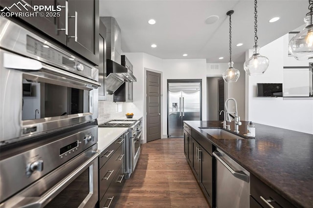 kitchen with dark wood finished floors, decorative backsplash, high end appliances, wall chimney range hood, and a sink