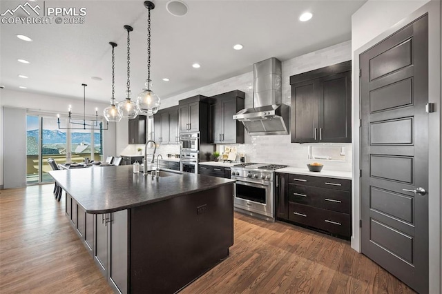 kitchen with decorative backsplash, wall chimney exhaust hood, appliances with stainless steel finishes, wood finished floors, and a sink