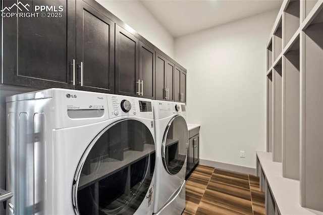 washroom featuring dark wood-style floors, washer and clothes dryer, cabinet space, and baseboards