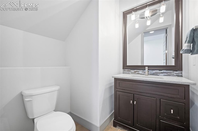 half bath with baseboards, decorative backsplash, toilet, vaulted ceiling, and vanity