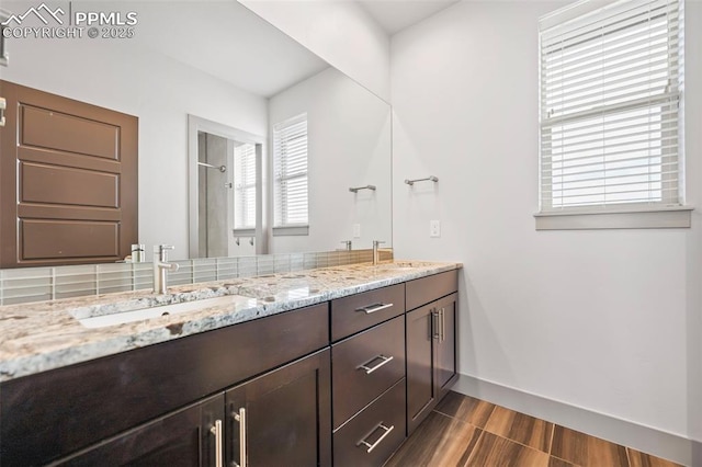 full bathroom with double vanity, baseboards, walk in shower, and a sink