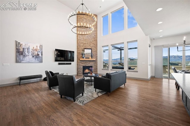 living room with baseboards, wood finished floors, a stone fireplace, a chandelier, and recessed lighting