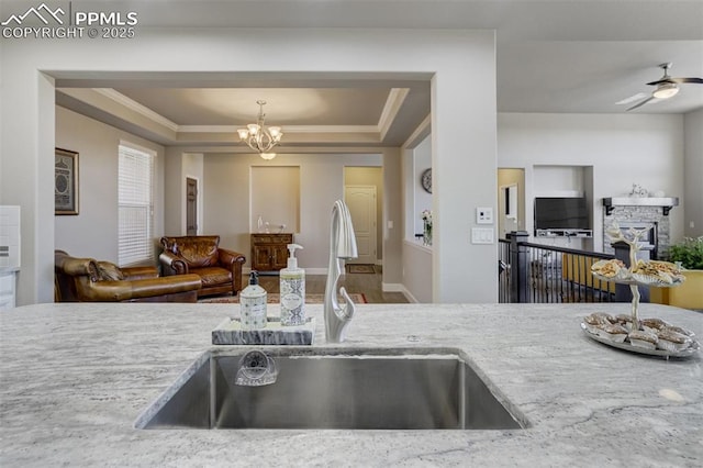 kitchen featuring a raised ceiling, open floor plan, light stone countertops, crown molding, and a sink