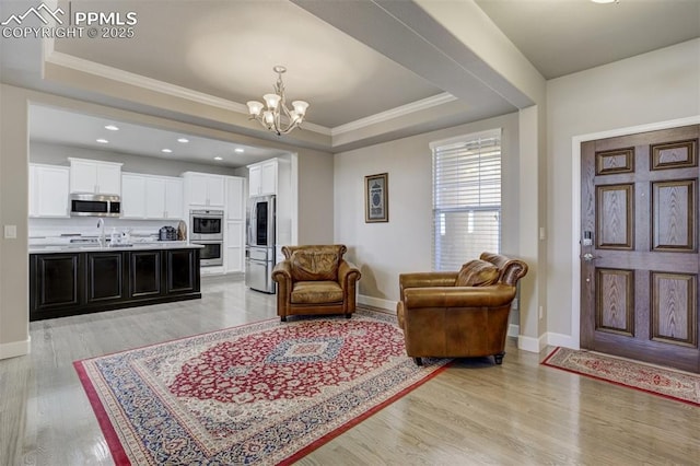 living room with crown molding, light wood-type flooring, a raised ceiling, and an inviting chandelier