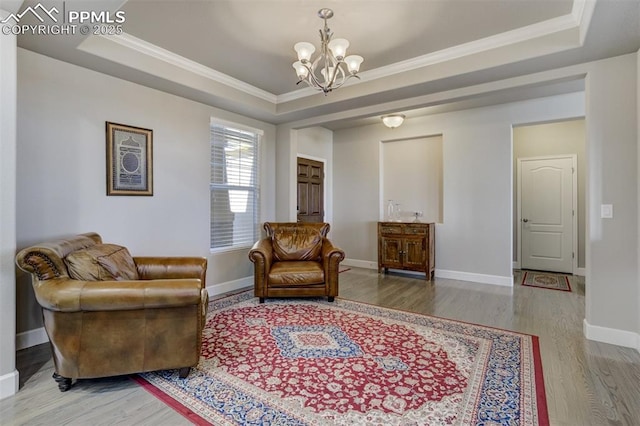 living area featuring an inviting chandelier, crown molding, a tray ceiling, and wood finished floors