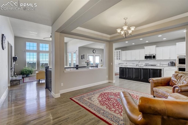 living area featuring a tray ceiling, crown molding, baseboards, and wood finished floors