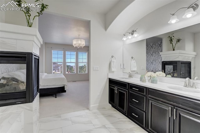 ensuite bathroom featuring a fireplace, a sink, marble finish floor, double vanity, and ensuite bath