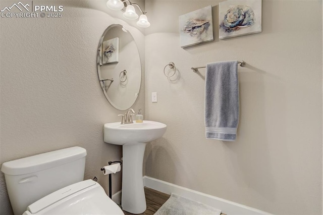 half bathroom featuring wood finished floors, toilet, and baseboards