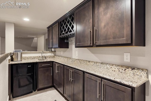 kitchen with recessed lighting, a sink, dark brown cabinetry, and light stone countertops