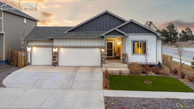 view of front of home featuring roof with shingles, an attached garage, board and batten siding, fence, and driveway