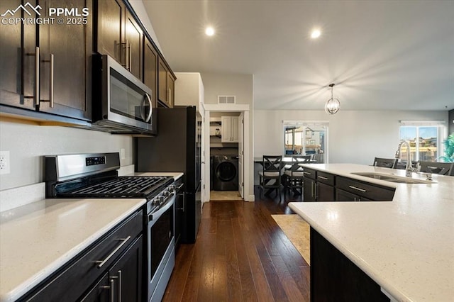 kitchen featuring appliances with stainless steel finishes, washer / clothes dryer, dark wood-style flooring, dark brown cabinets, and a sink