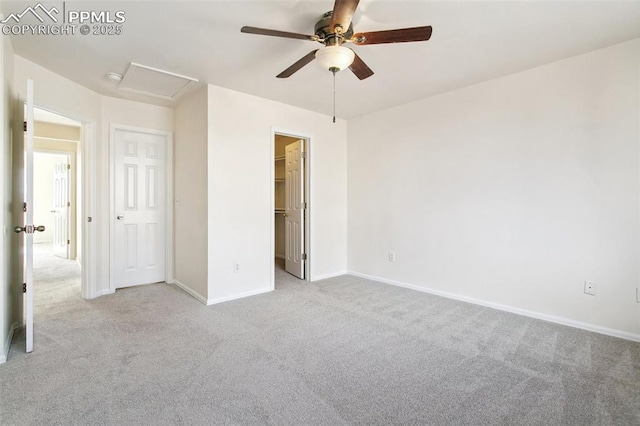 unfurnished bedroom with light carpet, a ceiling fan, baseboards, a walk in closet, and attic access