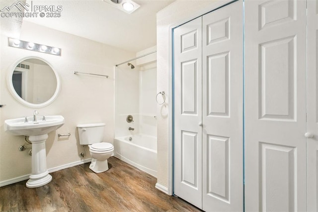 bathroom with toilet, wood finished floors, bathing tub / shower combination, baseboards, and a closet