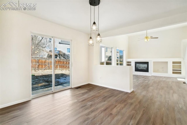 unfurnished dining area featuring dark wood-style floors, a glass covered fireplace, a wealth of natural light, and baseboards